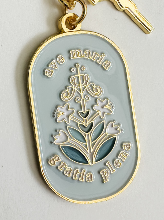 Light blue background of keychain with dark blue floral design and gold border