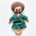 Toy figure of a person with a green dress and brown hair on a white background