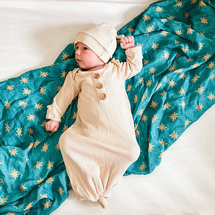 Baby in a beige outfit and hat lying on a teal blanket with star patterns