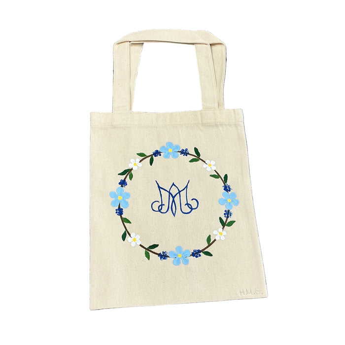 Beige tote bag with floral design on a floral-patterned fabric background