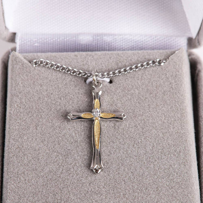 Silver and gold cross necklace on a gray cushion in a jewelry box