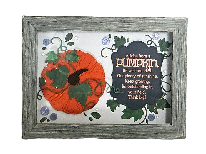 A framed autumn-themed art piece featuring a 3D orange pumpkin with green leaves next to a dark slate sign that reads 'Advice from a pumpkin' with inspirational text, set in a distressed gray wooden frame against a textured gray background.