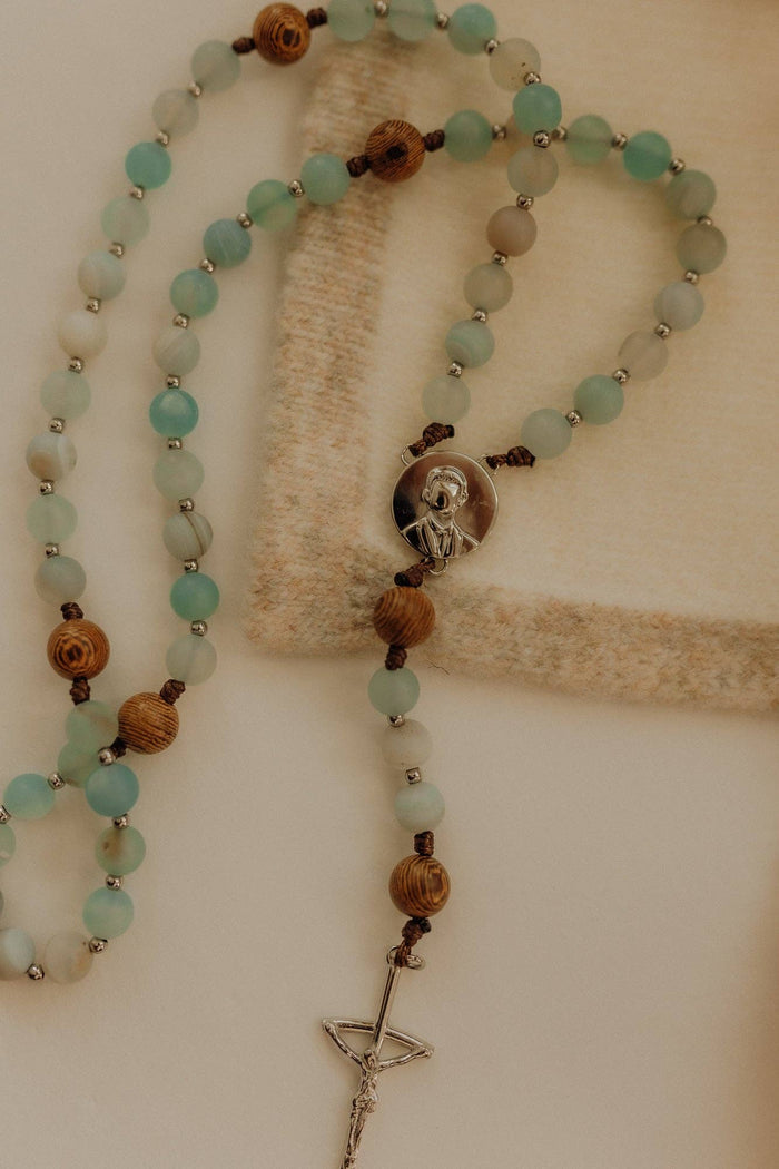 Rosary with turquoise and brown beads and a silver cross on a beige background