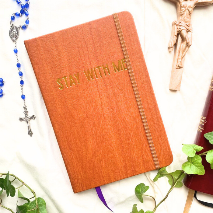 Orange book with 'Stay With Me' text, rosary, crucifix, and plant on a light background