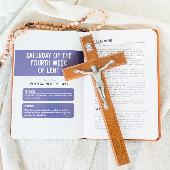 Open book with a wooden cross and rosary on a light fabric background