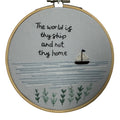 Embroidery hoop with text 'The world is thy ship and not thy home' and a sailboat on a gray background.