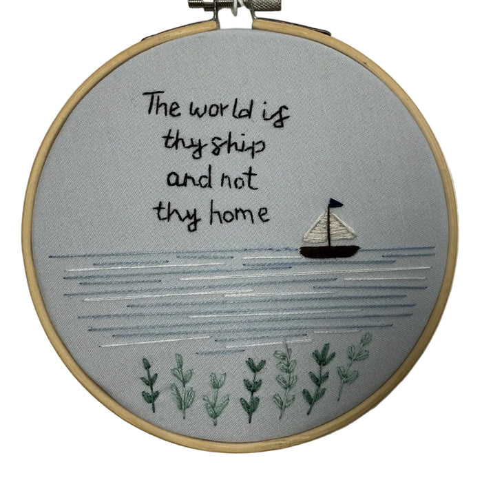 Embroidery hoop with text 'The world is thy ship and not thy home' and a sailboat on a gray background.